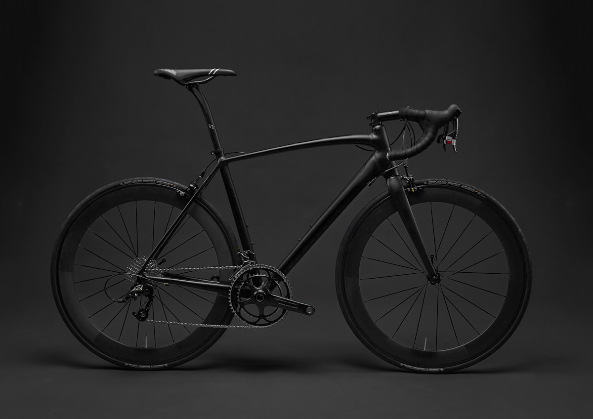 Stealth-black road bicycle with alloy wheels photographed in profile inside a minimalist studio setup