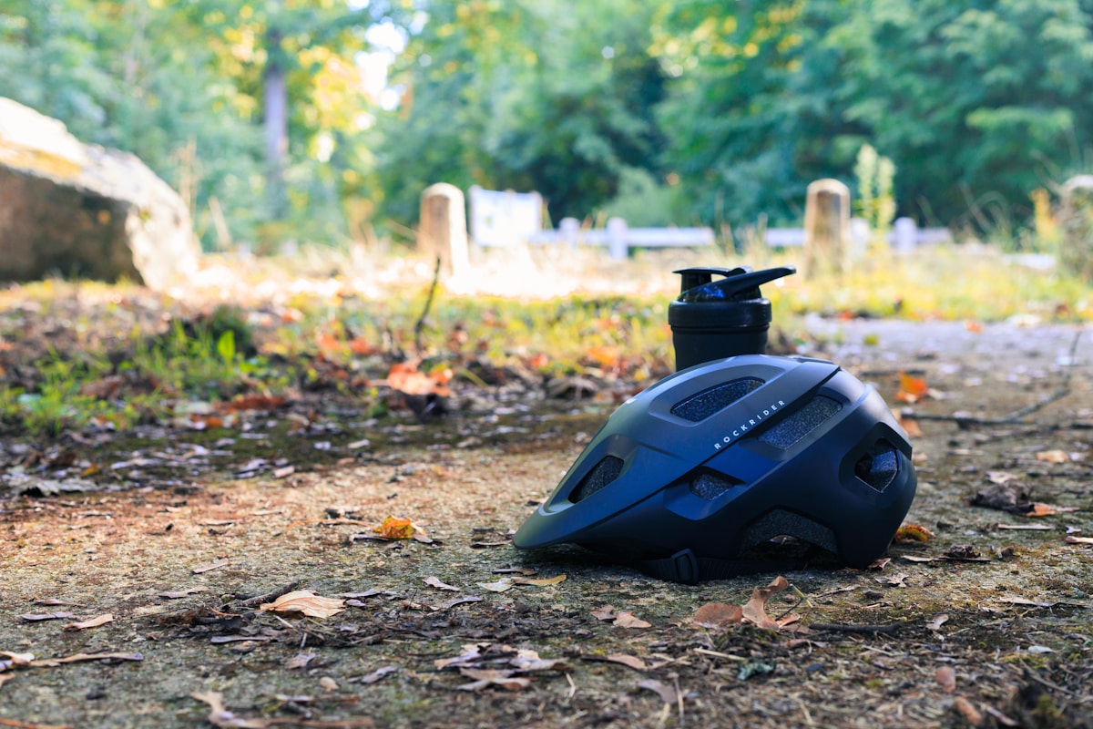 Matt navy cycling helmet and black water bottle on a forest trail bathed in sun