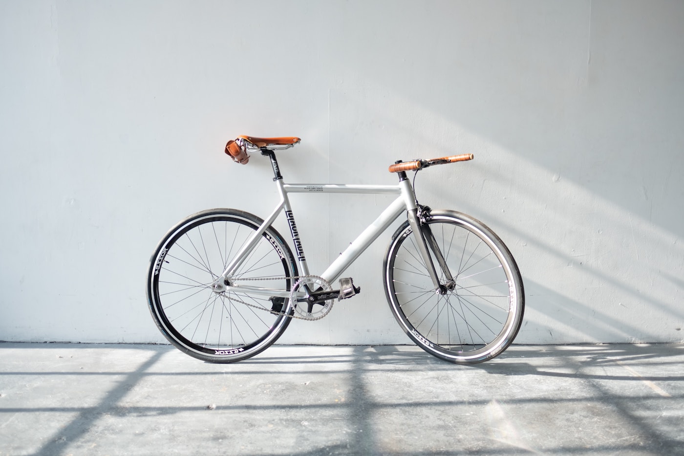 Urban commuter bicycle with tan leather saddle and deep-section rims against an off-white wall