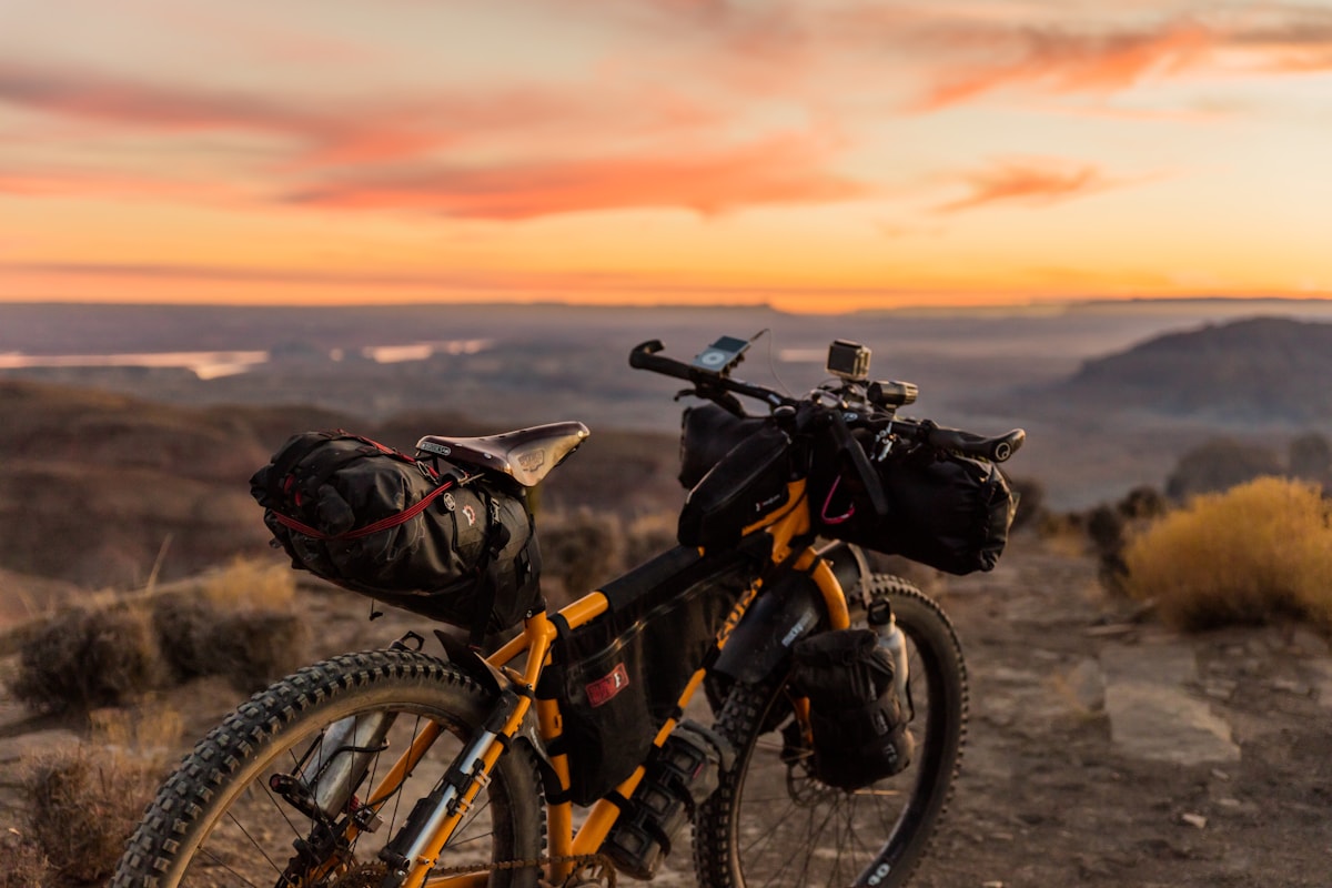 Bikepacking mountain bike laden with cockpit bags atop a dusty desert trail beneath a blazing sunset sky