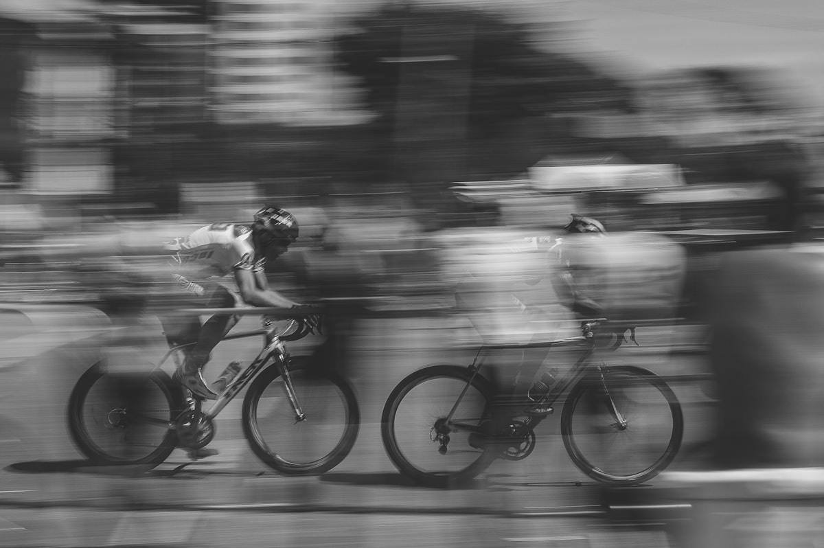 Black-and-white panning photograph of two road cyclists sprinting shoulder to shoulder